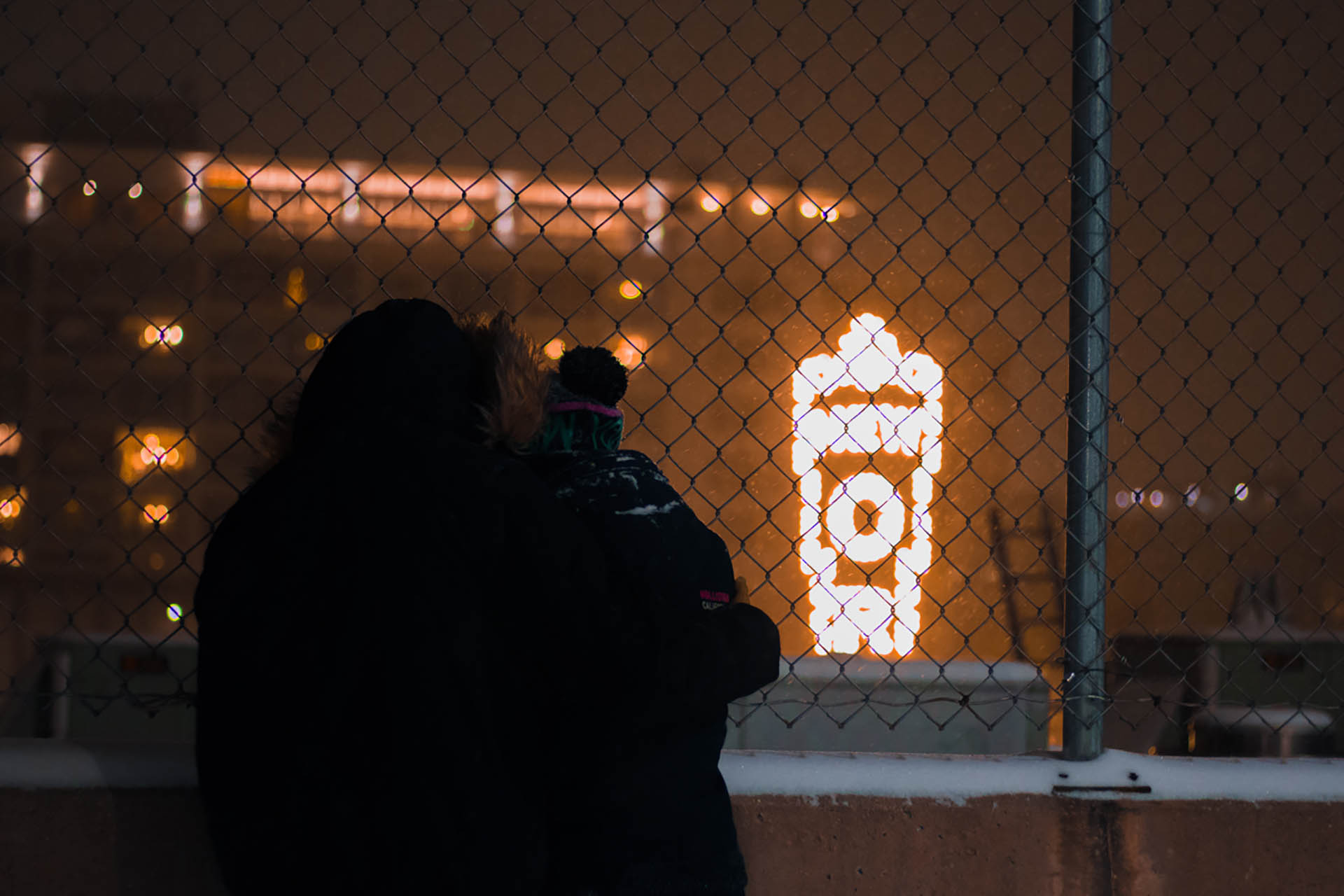 Young couple embracing in front of neon sign.