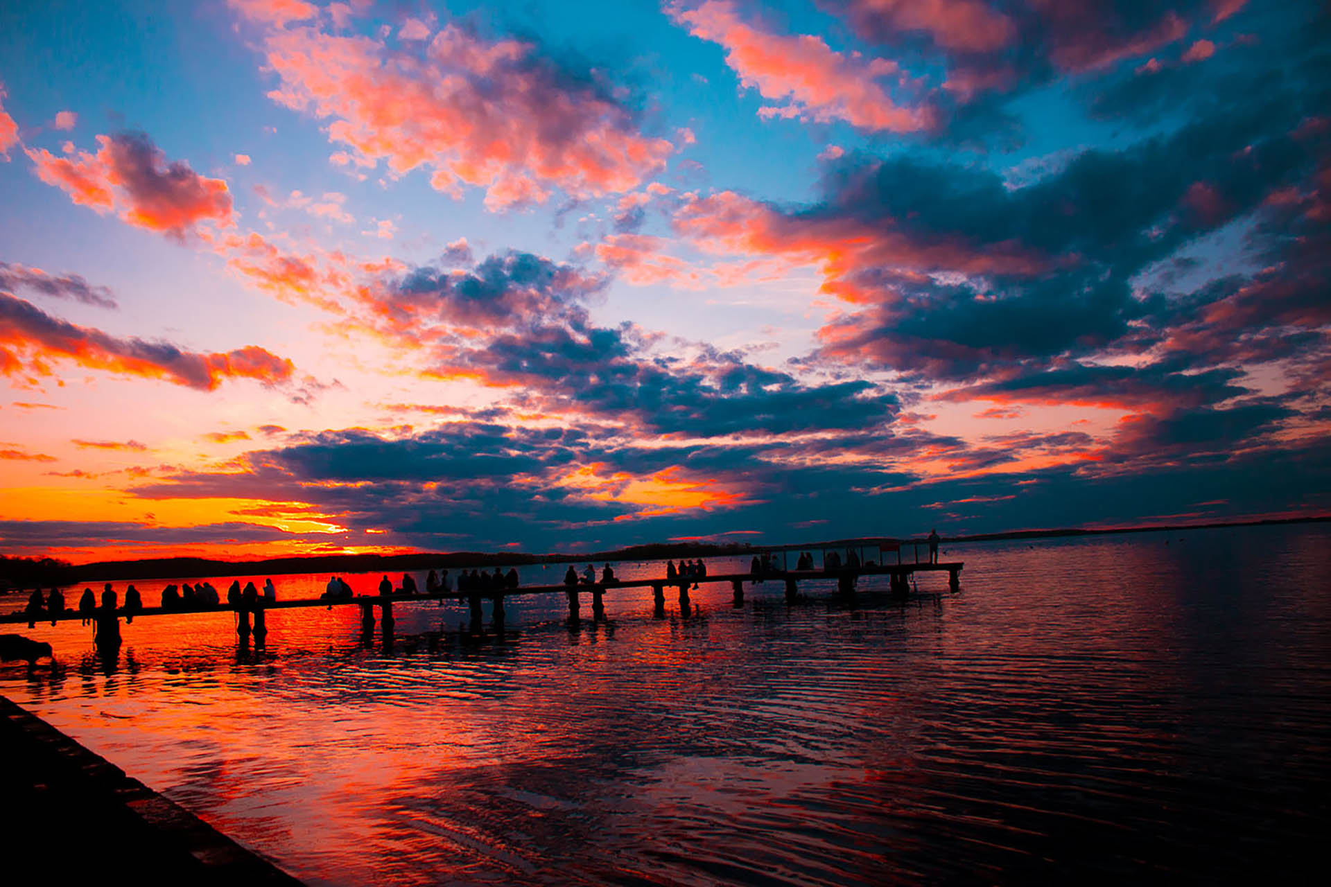 Alluringly colored dusk skyline, shimmering over a populated lakeside dock. 