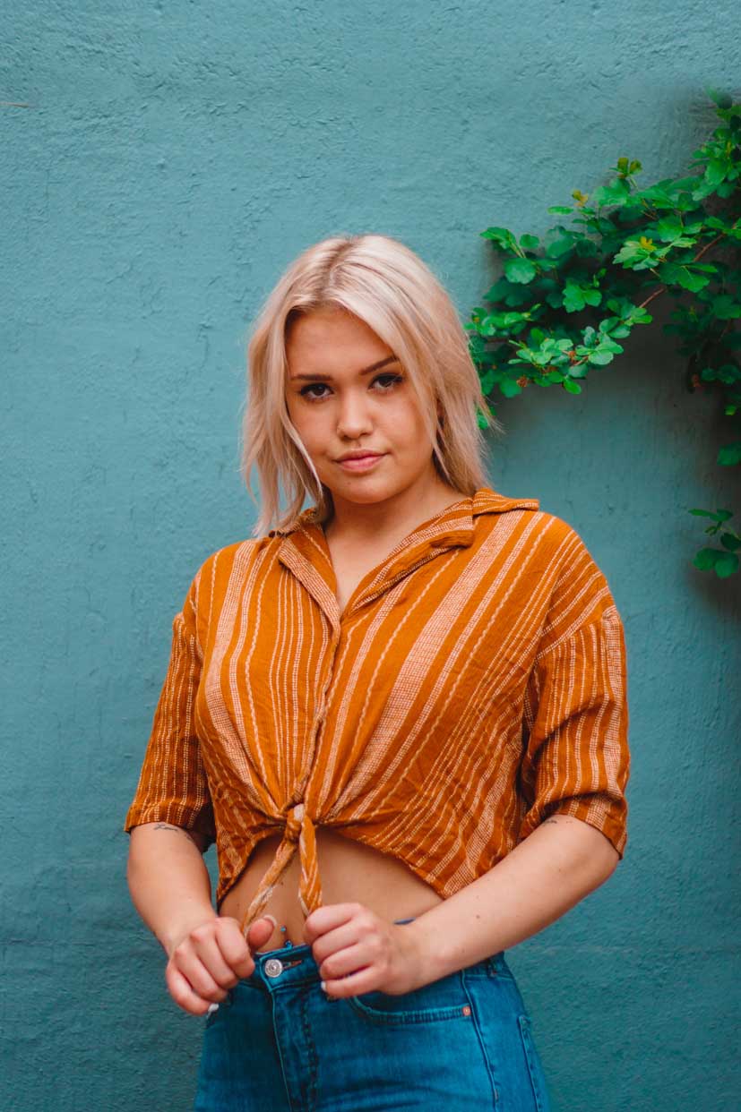 girl model photoshoot against blue wall waering orange shirt